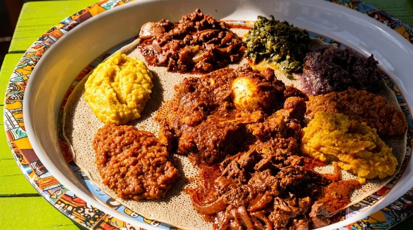 A colorful platter of Ethiopian food, including injera, stews, and vegetable dishes, on a green table.