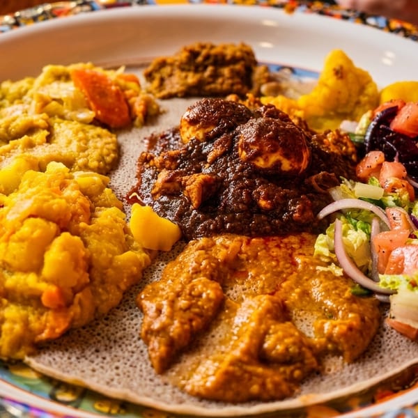 Colorful Ethiopian platter with injera bread, various stews, and fresh salad.
