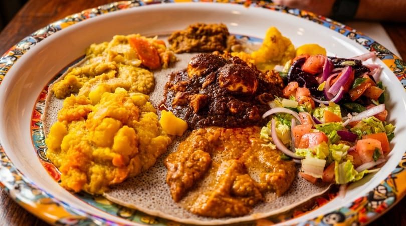 Colorful Ethiopian platter with injera bread, various stews, and fresh salad.