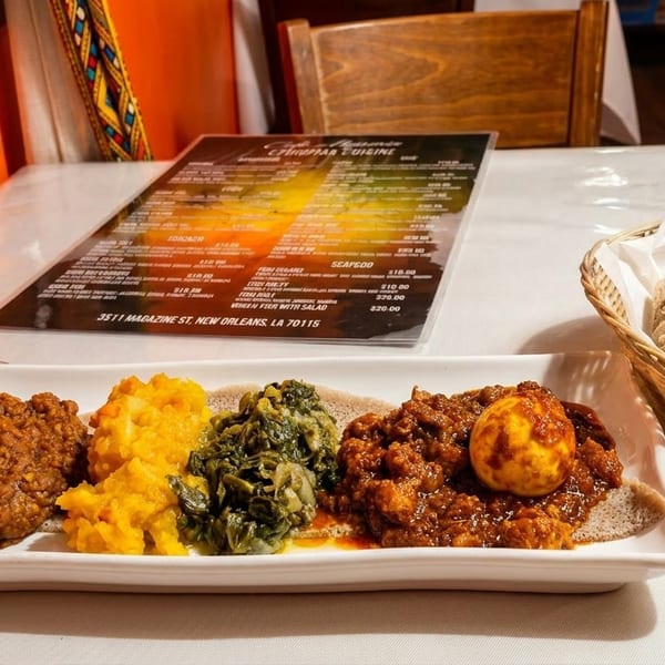 Ethiopian platter with injera, various stews, and a glass of red wine on a white tablecloth.