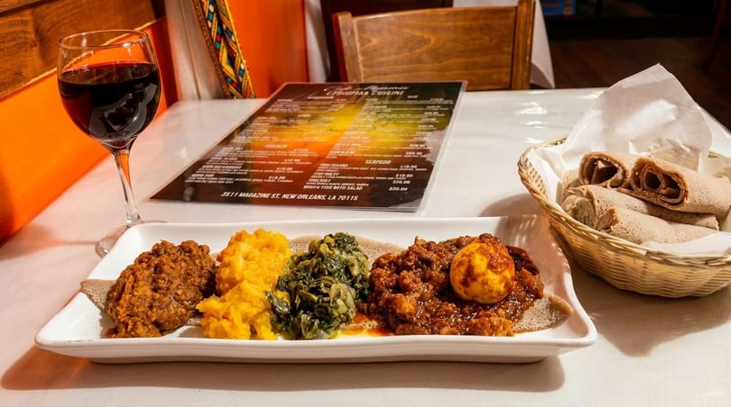 Ethiopian platter with injera, various stews, and a glass of red wine on a white tablecloth.