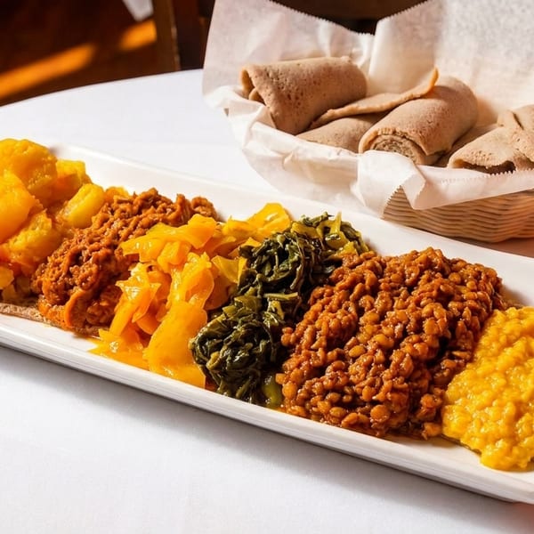 A long white platter of colorful Ethiopian dishes, including lentils, greens, and potatoes, with injera bread.
